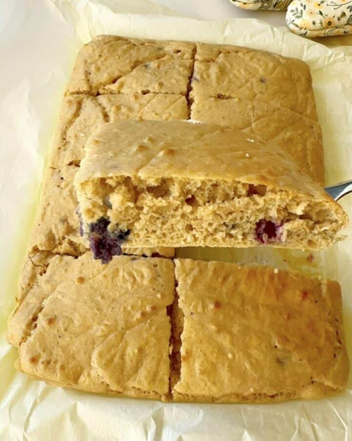 A thick, fluffy squarish sheet pan blueberry pancake in the foreground with several behind in a pan.