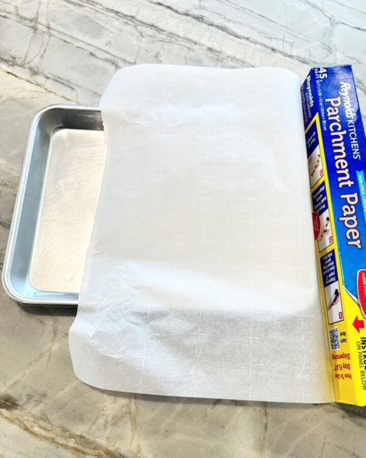 Silver sheet pan with roll of white parchment paper.