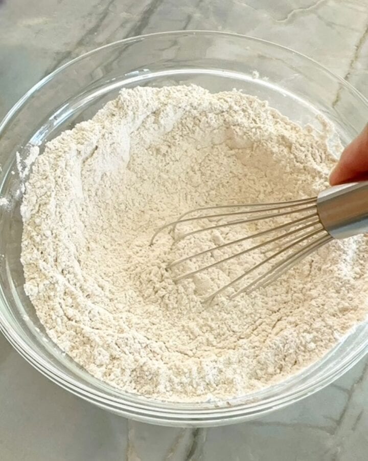 Whisking flours, protein powder, and spices in a clear bowl for pancakes.