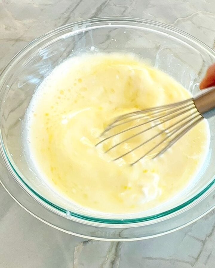 Whisking milk, Greek yogurt, eggs, oil, etc. in a clear bowl to make protein pancakes (sheet-pan).