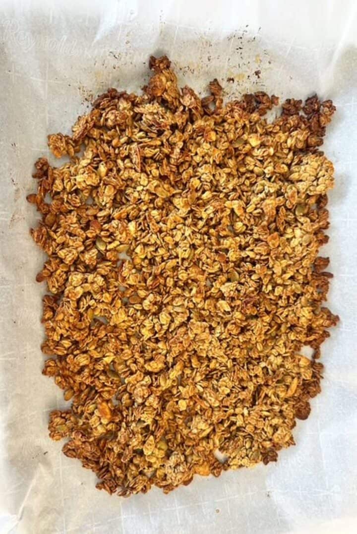 Golden brown layer of baked granola on a white parchment sheet.