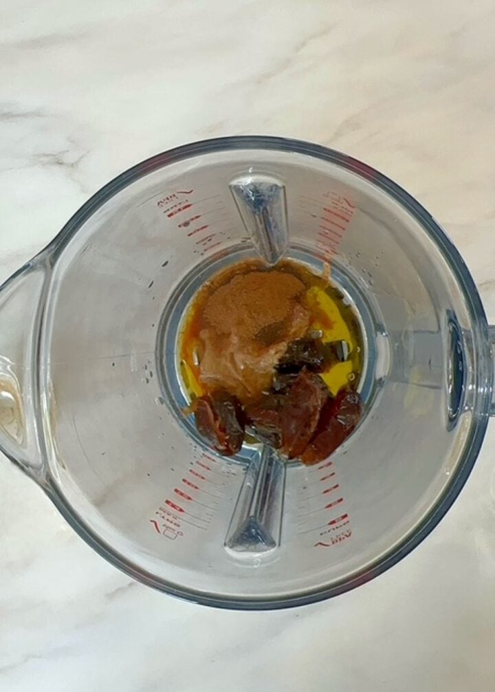 Dark ingredients including dates and almond butter in a blender container with lid off.