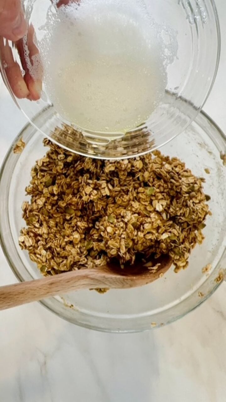 An egg white is poured over sticky oat, nut, seed granola mixture.
