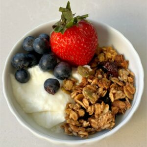 White bowl with white plain yogurt topped with date-paste sweetened granola and berries.