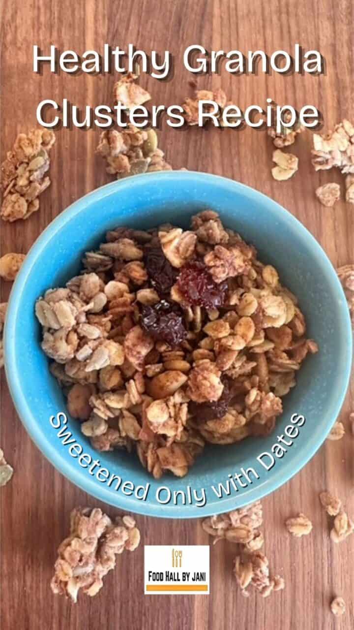 A green-blue bowl full of golden, oat and seed granola on a wooden board.