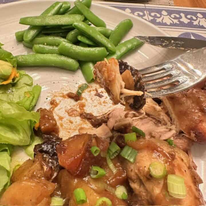 A fork holds a bite of tender chicken meat with a soft prune.
