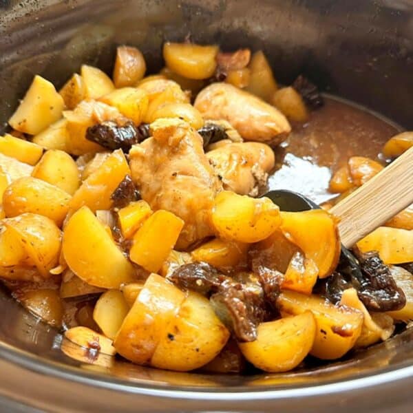 Cooked boneless chicken, yellow potatoes, and dark prunes are bathed in juices in a black slow cooker liner.