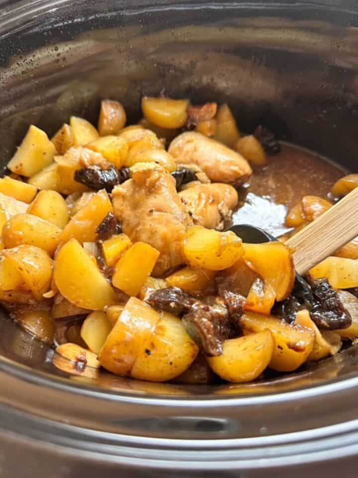 Tender baby potatoes and dark, soft fruit in juices of slow-cooked chicken dish.