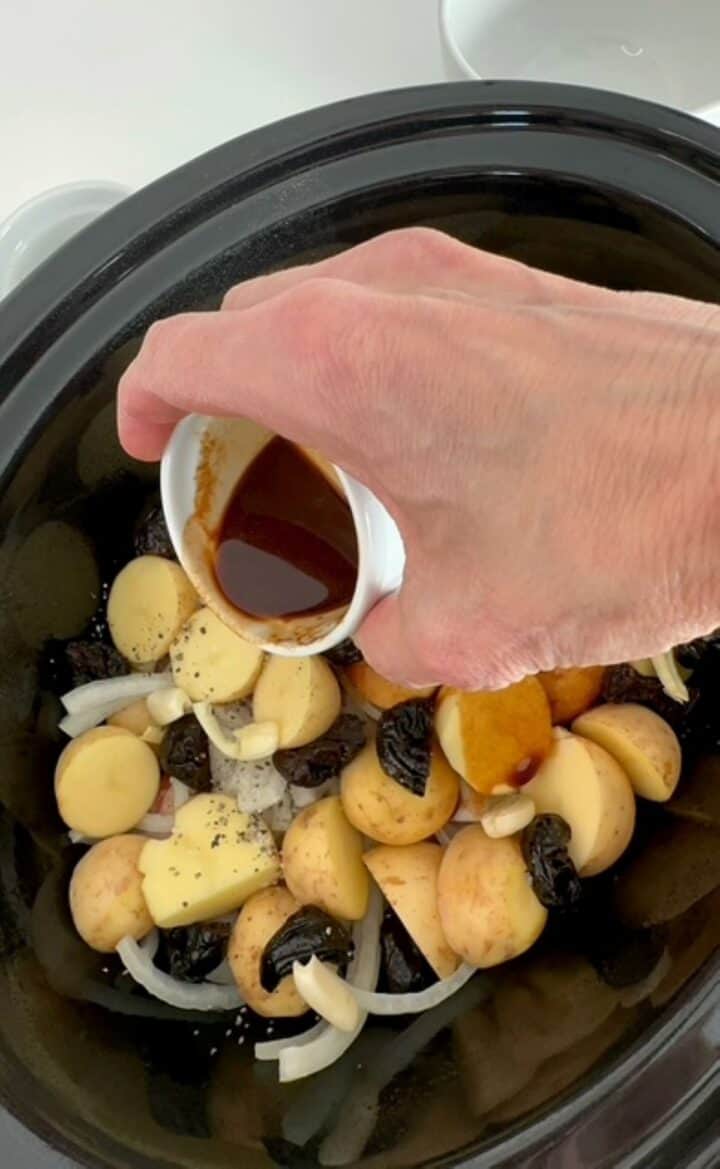 Dark brown soy sauce with ginger is poured over chicken potatoes onions in a slow cooker.