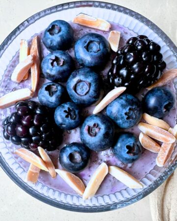 Round bowl of blueberry chia pudding topped with dark berries.