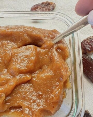 Thick, caramel colored date paste in clear, square dish with a spoon in it.