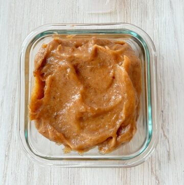 Thick, caramel-colored date paste fills a square glass storage container.