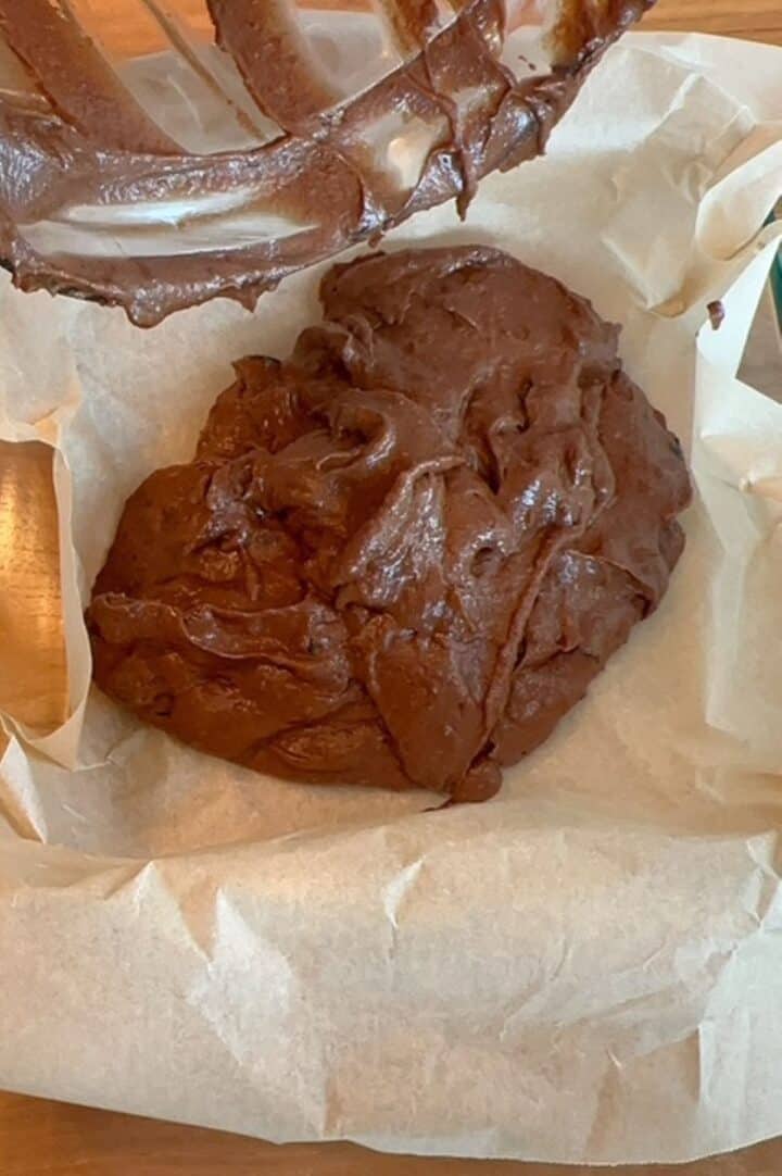 Brown chocolate brownie batter is poured into a square glass pan lined with parchment.