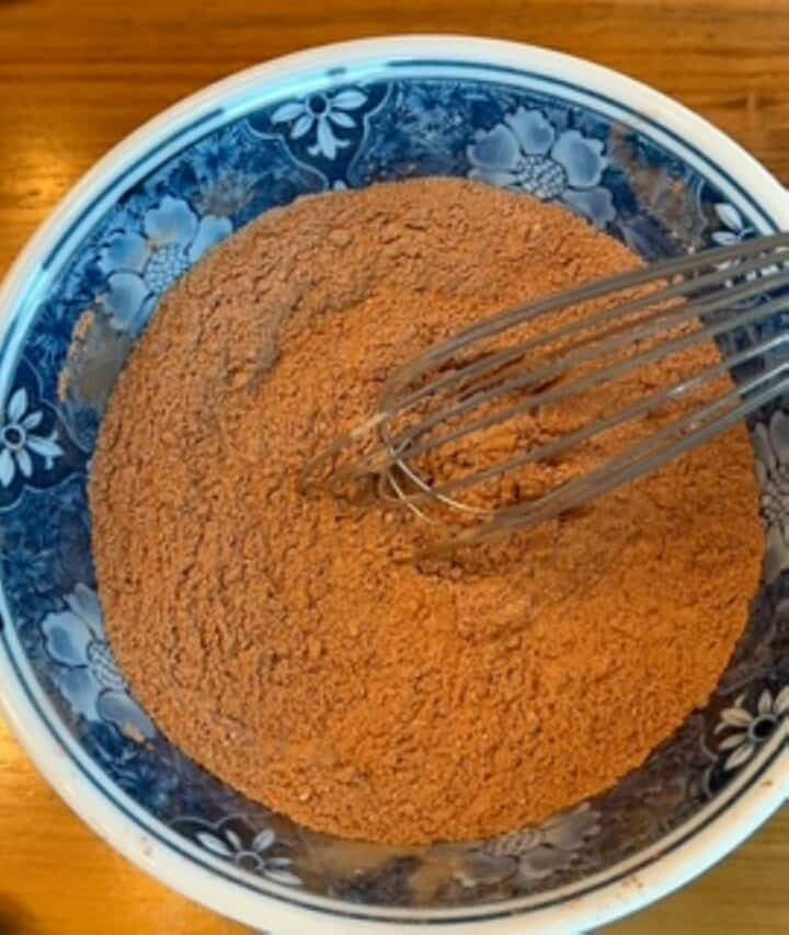 Blue ceramic bowl with cocoa powder and flour mixture for date paste brownies.
