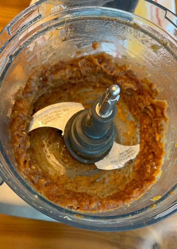 Open food processor showing dates pulverized into brown paste.