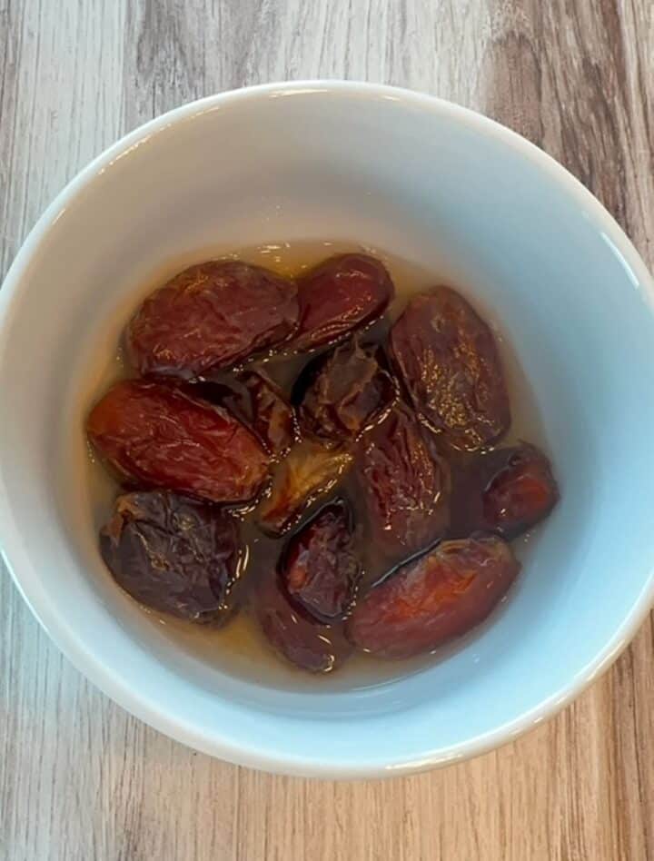 White bowl holds large brown dates soaking in water.