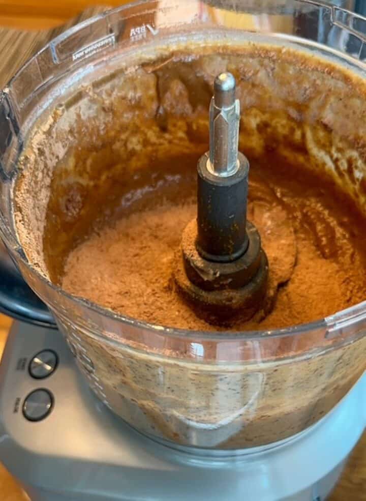 Open food processor with brown wet batter and dry cocoa powder on top.