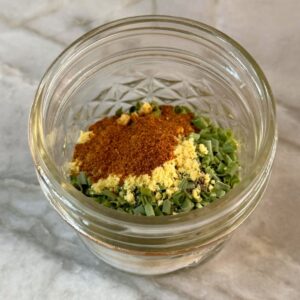 Close-up of a jar with burger seasoning ingredients including spices and herbs.