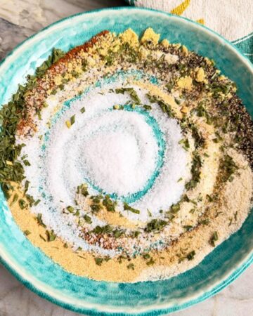 Burger seasoning mix with garlic powder, black pepper, herbs, mustard, and salt in a blue bowl.