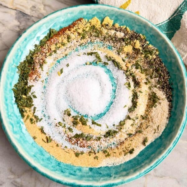 Burger seasoning mix with garlic powder, black pepper, herbs, mustard, and salt in a blue bowl.