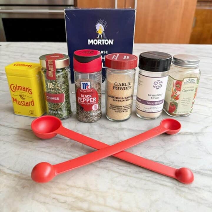 A row of spice jars with red measuring spoons on a kitchen counter.