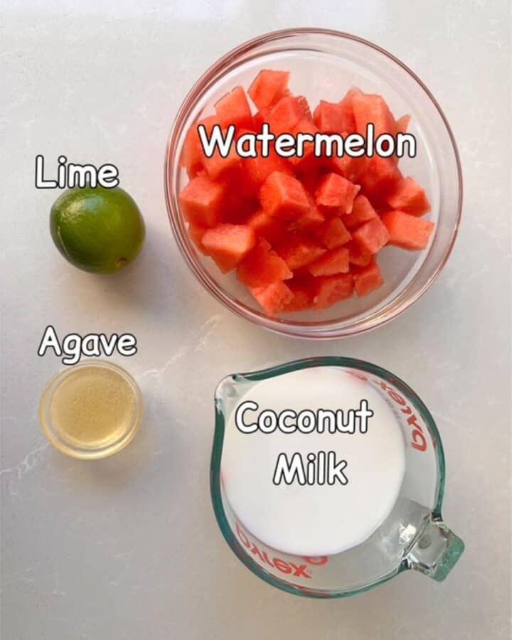 Bowl of red watermelon chunks, a green lime, amber agave, and white coconut milk.