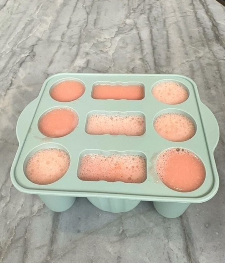 Creamy pink watermelon-coconut milk puree fills the wells in a light green silicone popsicle mold.