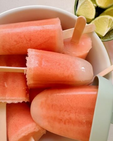 Pink watermelon popsicles with white tips (from coconut) milk are piled into a white ceramic bowl.