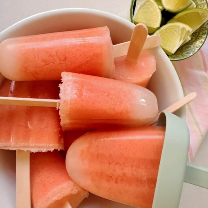 Pink watermelon popsicles with white tips (from coconut) milk are piled into a white ceramic bowl.