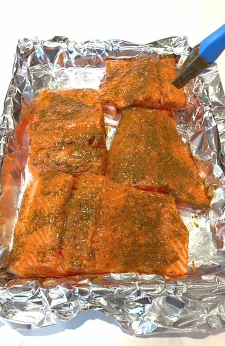 Fresh, raw salmon fillets coated with honey Dijon dill glaze on foil, ready to bake.