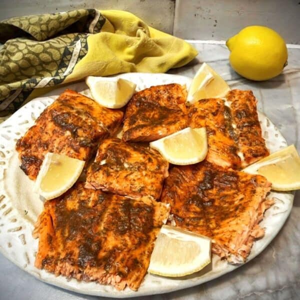 A beige platter loaded with baked Honey-Dijon-Dill glazed salmon fillets, with wedges of yellow lemon as a garnish.