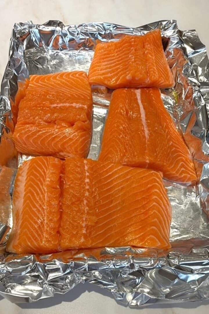 Raw salmon fillets on aluminum foil, ready for brushing with honey-mustard glaze.