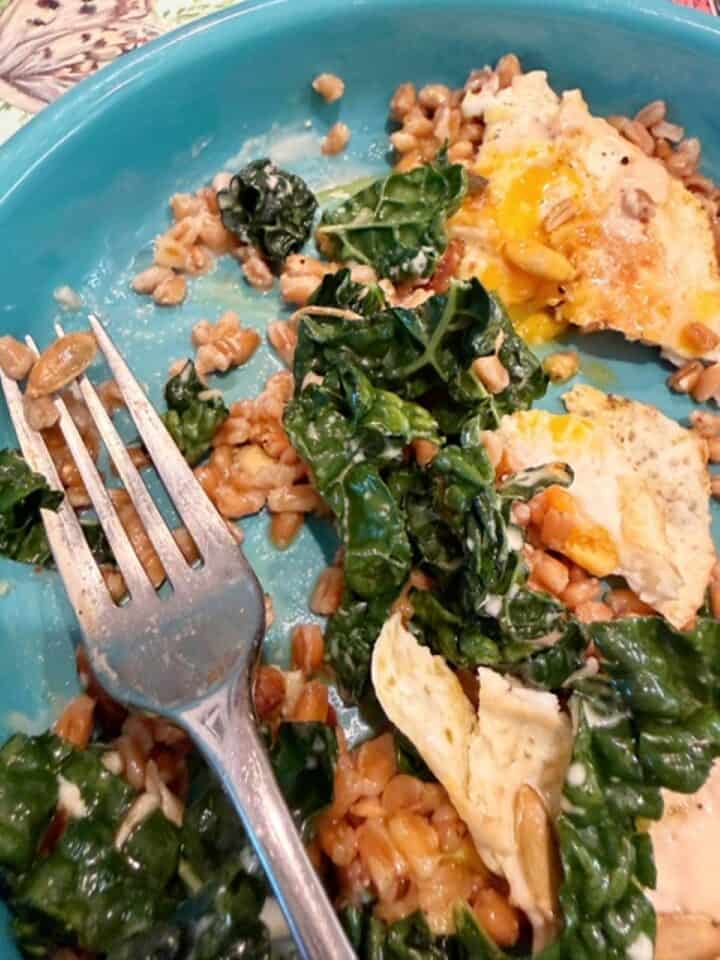 Healthy sauteed kale with eggs and farro on a blue plate.