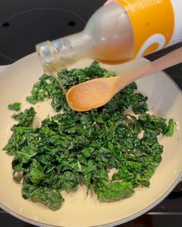 Freshly sautéed kale being seasoned with balsamic vinegar in a skillet.