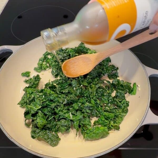 Freshly sautéed kale being seasoned with balsamic vinegar in a skillet.