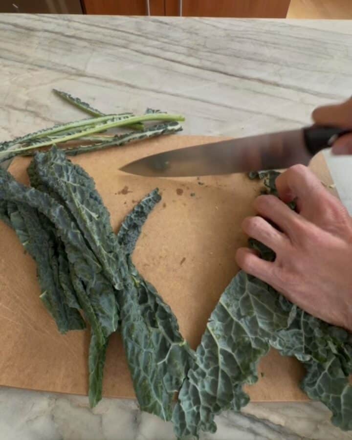 Person slicing kale leaves on a wooden cutting board.