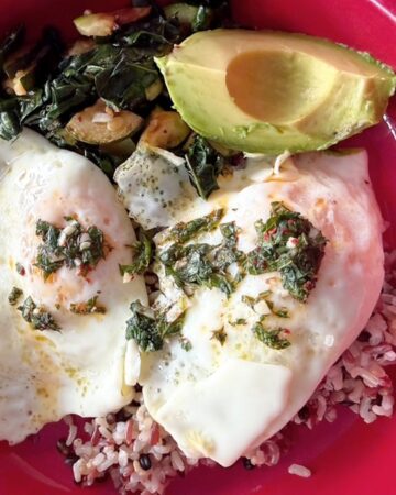 Healthy breakfast bowl with eggs, kale, zucchini, and avocado on rice.