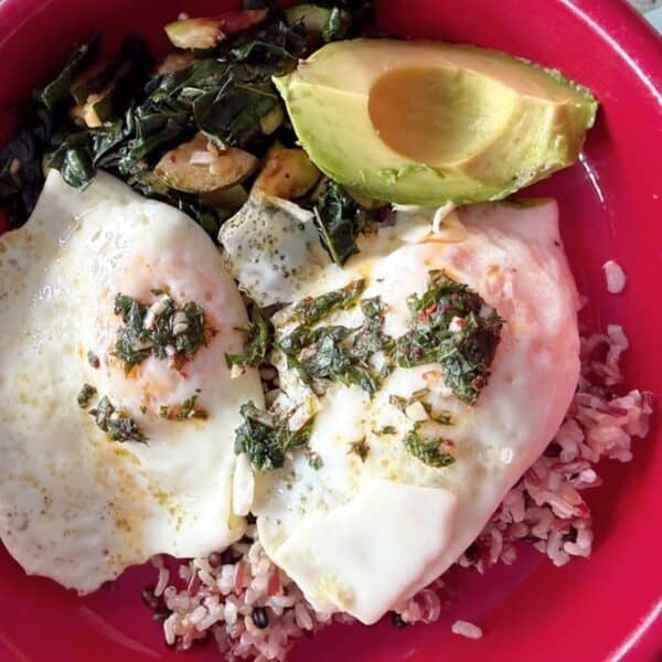 Healthy breakfast bowl with eggs, kale, zucchini, and avocado on rice.