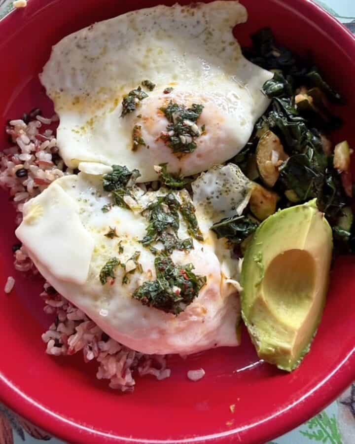 Healthy breakfast bowl with eggs, kale, zucchini, grainy rice blend, and avocado.