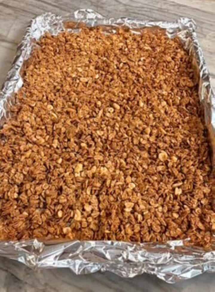Homemade crunchy peanut butter granola cooling in foil-lined sheet pan.
