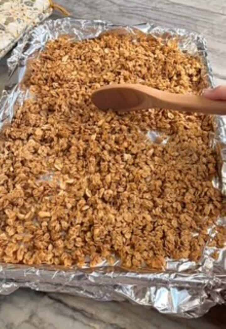 Stirring peanut butter granola halfway through baking with a wooden spoon.