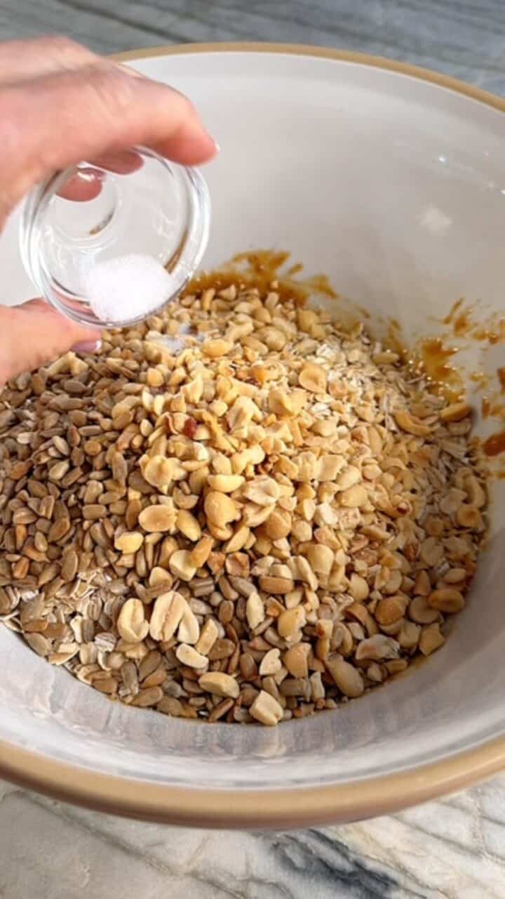 Adding oats, nuts, seeds, and salt to bowl with wet ingredients for peanut butter granola.