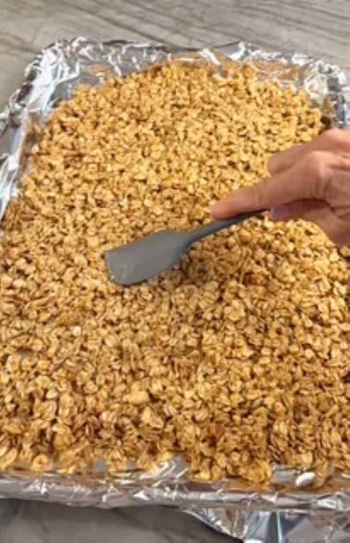 Raw peanut butter granola spread on foil with a hand spreading it with a spatula.