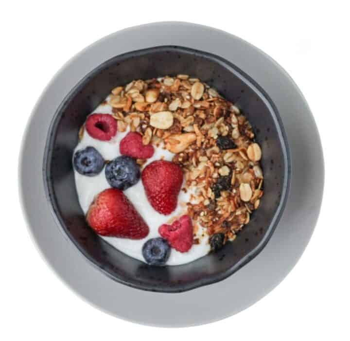Bowl of plain yogurt with red berries and blueberries and peanut butter granola.
