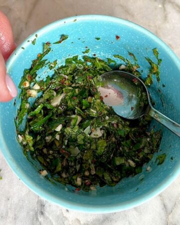 Close-up of mint gremolata in a blue bowl with a spoon.