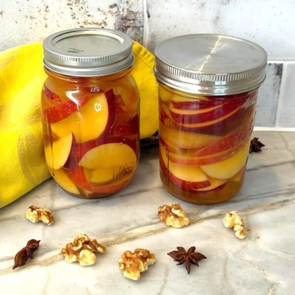 Two jars of pickled apples with spices on a marble surface.