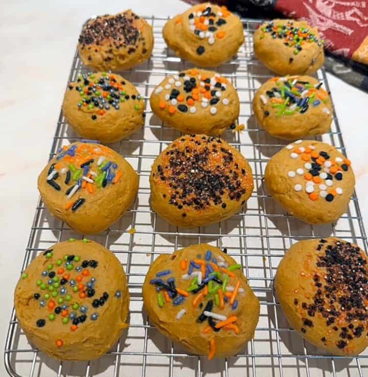 Light orange pumpkin ricotta cookies decorated with Halloween sprinkles on a cooling rack.