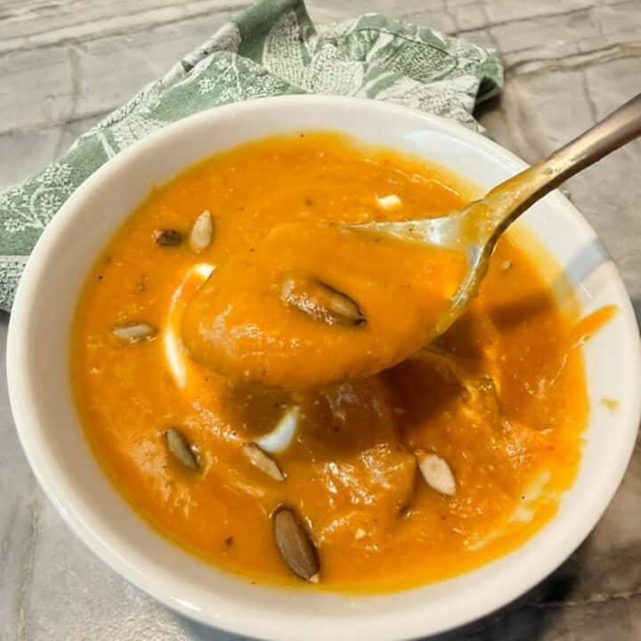 Thick, velvety butternut squash soup in a white bowl sprinkled with pumpkin seeds.