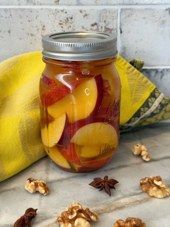 Jar of pickled apples with star anise an lemon peel for flavor.