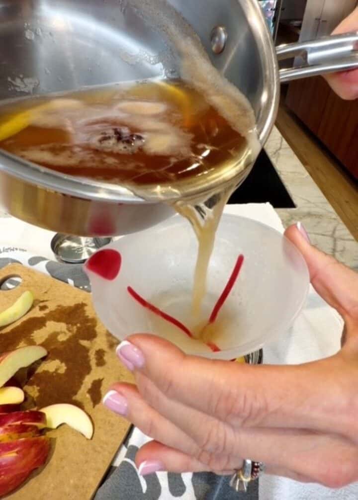 Pouring hot brine into a mason jar filled with apple slices.